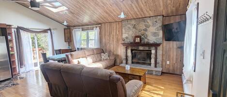 A spacious living room with a fireplace, wooden flooring, and a ceiling fan.