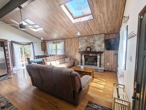 A spacious living room with a fireplace, wooden flooring, and a ceiling fan. - Quiet Poconos Chalet with Loft Lounge (ALBRIGHTSVLLE)