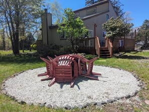 A patio area with a circular seating arrangement, a wooden deck, and a house in the background. - Quiet Poconos Chalet with Loft Lounge (ALBRIGHTSVLLE)