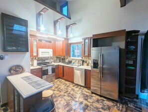 A kitchen with wooden cabinets, a stainless steel refrigerator, a microwave, and a patterned floor. - Quiet Poconos Chalet with Loft Lounge (ALBRIGHTSVLLE)