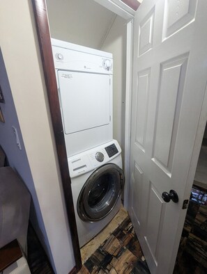 Une petite buanderie équipée d’un lave-linge et d’un sèche-linge Samsung à chargement frontal, d’une porte en bois et d’un sol à motifs.