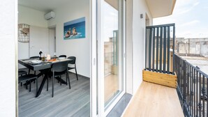 Un balcon doté d’un plancher en bois et d’une rambarde noire, un coin repas avec une table et des chaises, et un tableau accroché au mur.