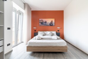 Una camera da letto moderna con un grande letto, un dipinto raffigurante un tramonto e vista sul mare dalla finestra.