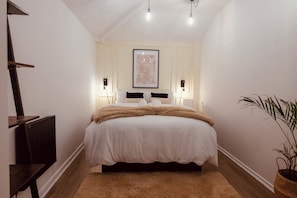 Une chambre à coucher avec un lit, des lampes de chevet, un tableau encadré au mur, un radiateur et une plante en pot.