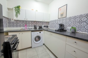A compact kitchen with a washing machine, microwave, and coffee maker. - 2-4 Thomas Street House  (Manchester)