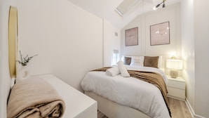 Un dormitorio moderno con una cama, mesitas de noche, un espejo y obras de arte en la pared.