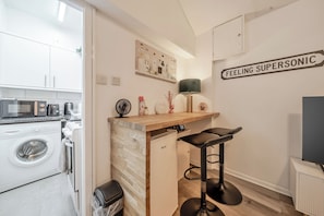 Une cuisine compacte équipée d’un lave-linge, d’un four à micro-ondes et d’un évier. On y trouve également un petit coin bar avec des tabourets et une lampe fixée au mur.