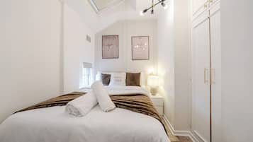 A bedroom with a bed, a nightstand, a lamp, a wardrobe, and two framed pictures on the wall.