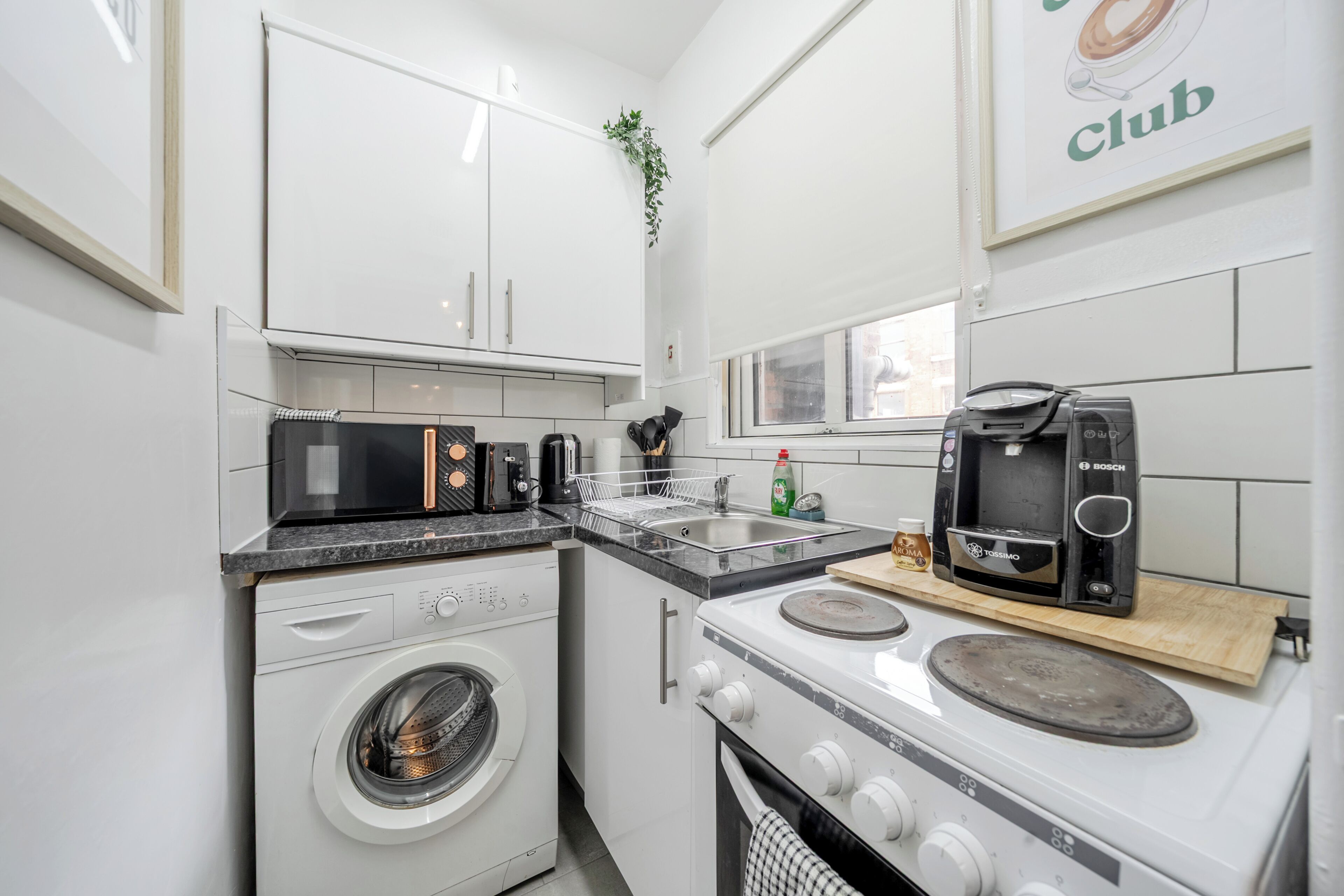A compact kitchen with a washing machine, microwave, coffee machine, and a small oven.