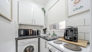 Cocina compacta equipada con lavadora, microondas, cafetera y horno pequeño.