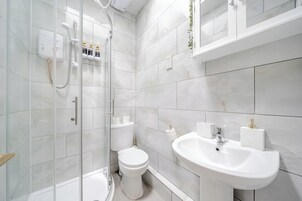 Egy modern fürőszoba, melyben üvegfalas zuhanyzó, WC és mosdókagyló található, a mosdókagyló felett pedig tükör van.