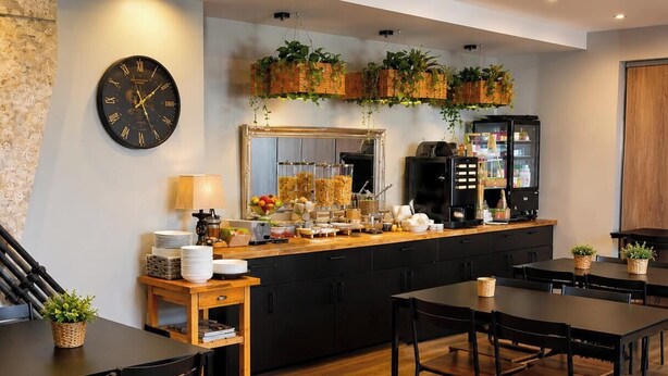 A modern kitchen with a wooden countertop, black cabinets, a clock, and hanging plants.