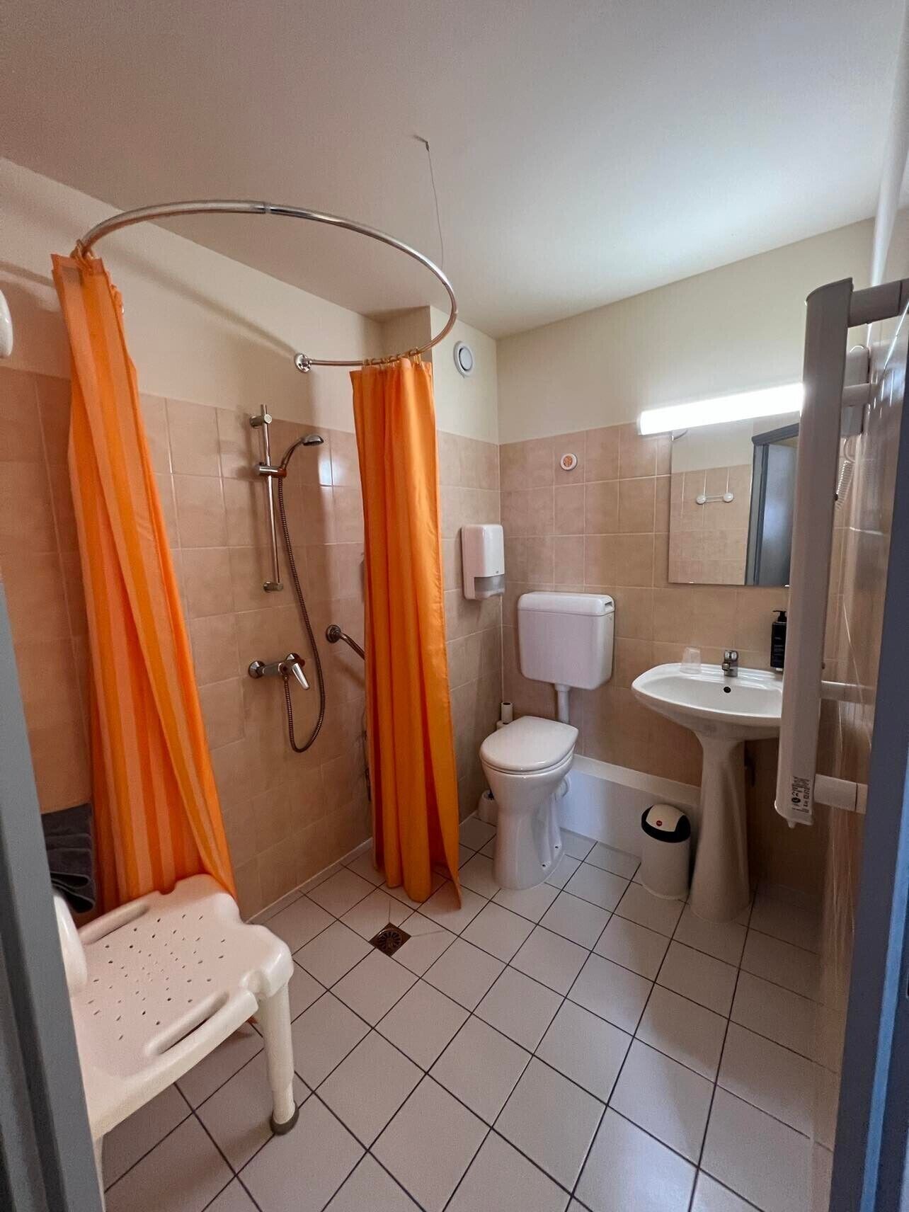 Un baño con ducha, inodoro, lavabo y una silla.
