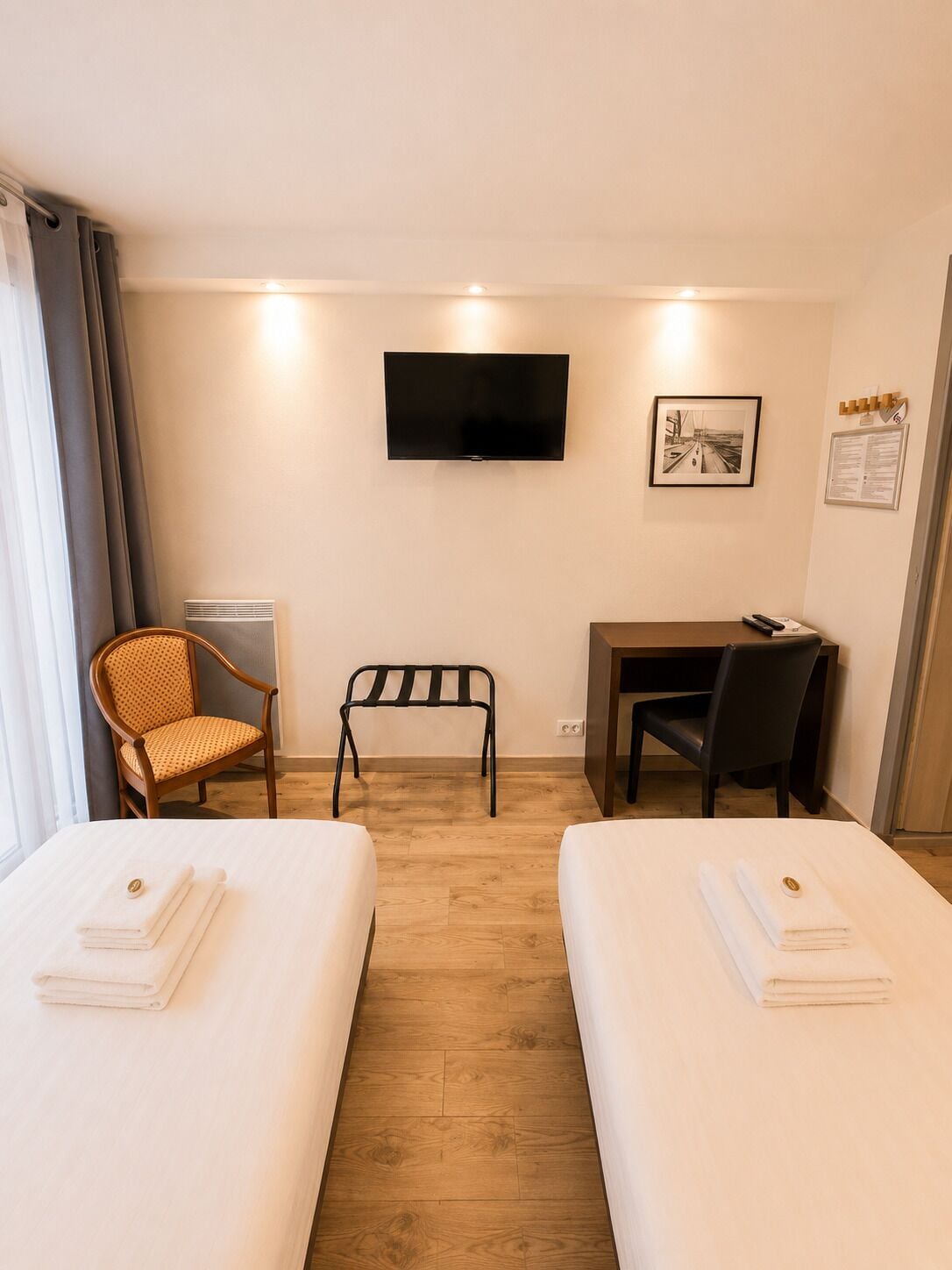 Habitación de hotel con dos camas, un escritorio, una silla, un televisor y un cuadro en la pared.