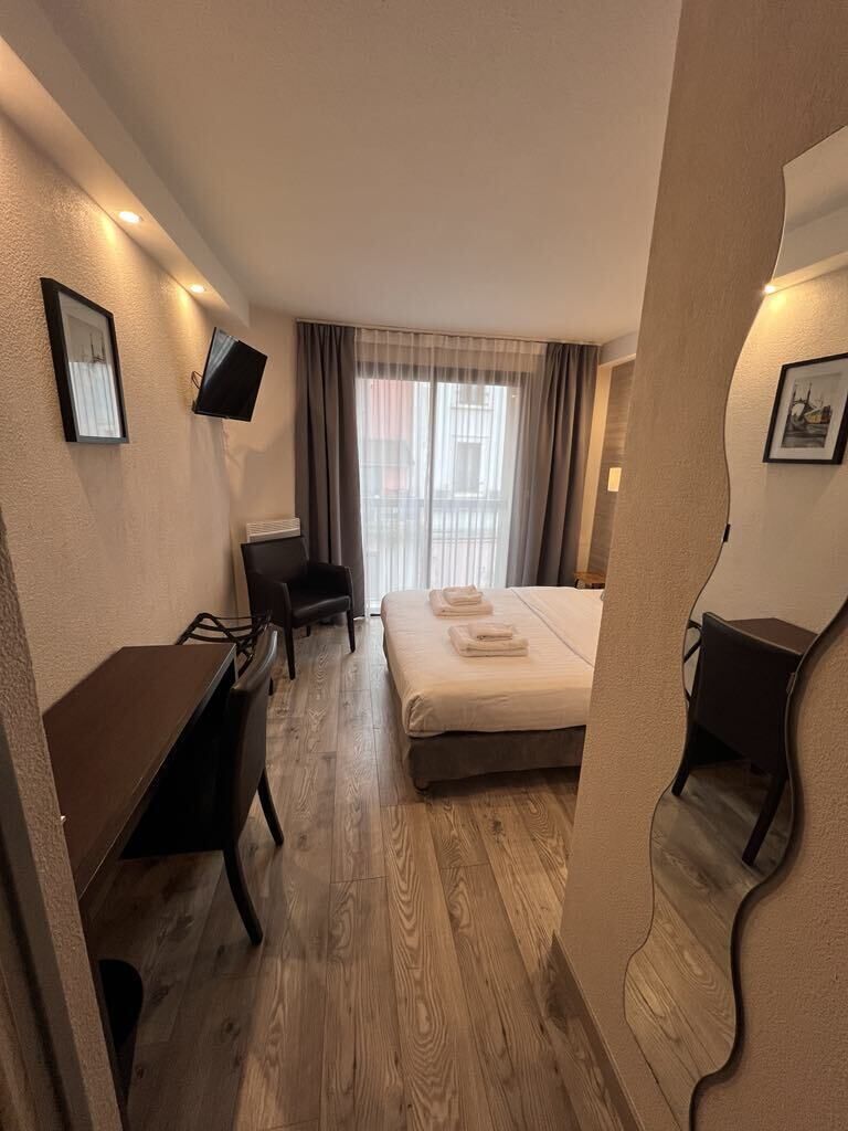 A hotel room with a bed, a desk, a chair, a TV, and a window with curtains.