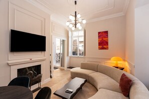 A living room with a flat-screen TV, a fireplace, a sofa, a coffee table, and a modern chandelier.