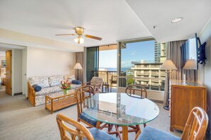 Ein Hotelzimmer mit Balkon, einem runden Glastisch, Korbstühlen, einer Couch und einem Deckenventilator.