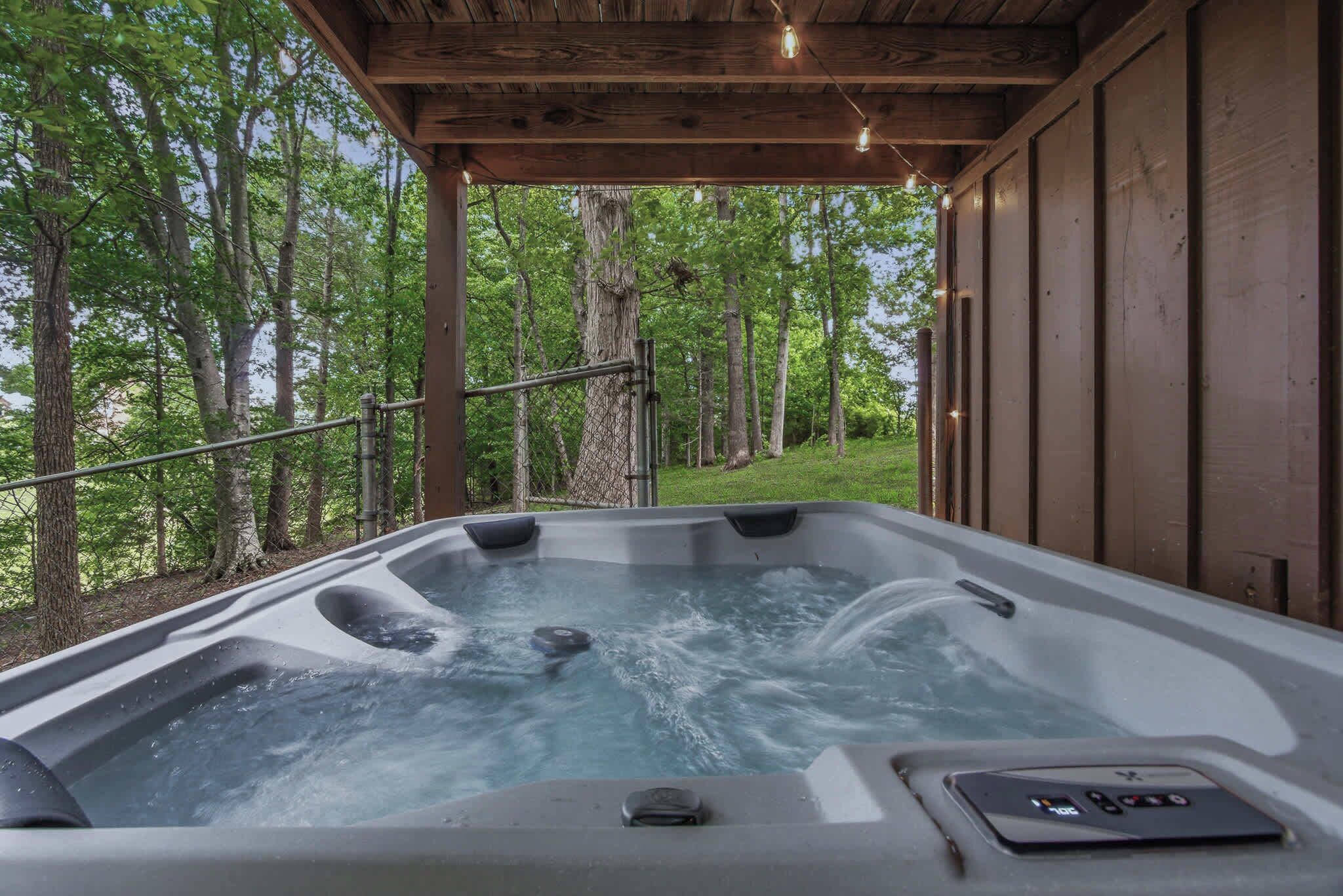 Un bain à remous doté d’une terrasse en bois, entouré d’arbres, et muni d’un panneau de commande sur le côté.
