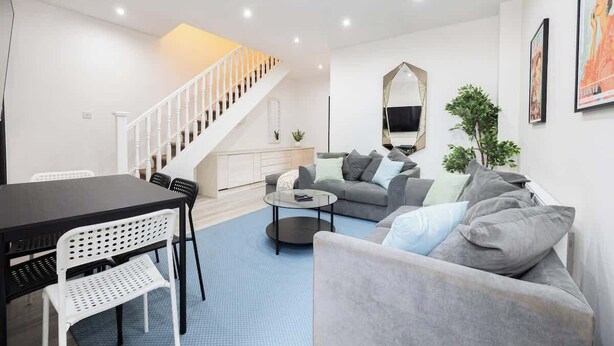 Un salon moderne avec un escalier, un coin repas et un ensemble de canapés.