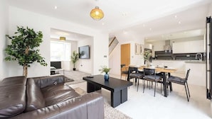 Ein modernes Wohnzimmer mit einer Ledersofa, einem Esstisch und Stühlen, einer Küchenzeile mit weißen Schränken sowie einer Treppe zu einer weiteren Ebene.
