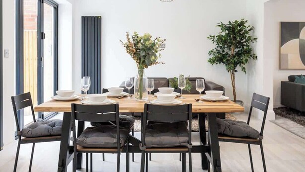 Ein moderner Essbereich mit einem Holztisch, gedeckt für sechs Personen, schwarzen Stühlen und einer Blumenvase.