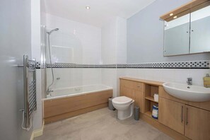 Un bany modern amb dutxa envidriada, banyera independent, vàter i un moble de tocador de fusta amb un lavabo.