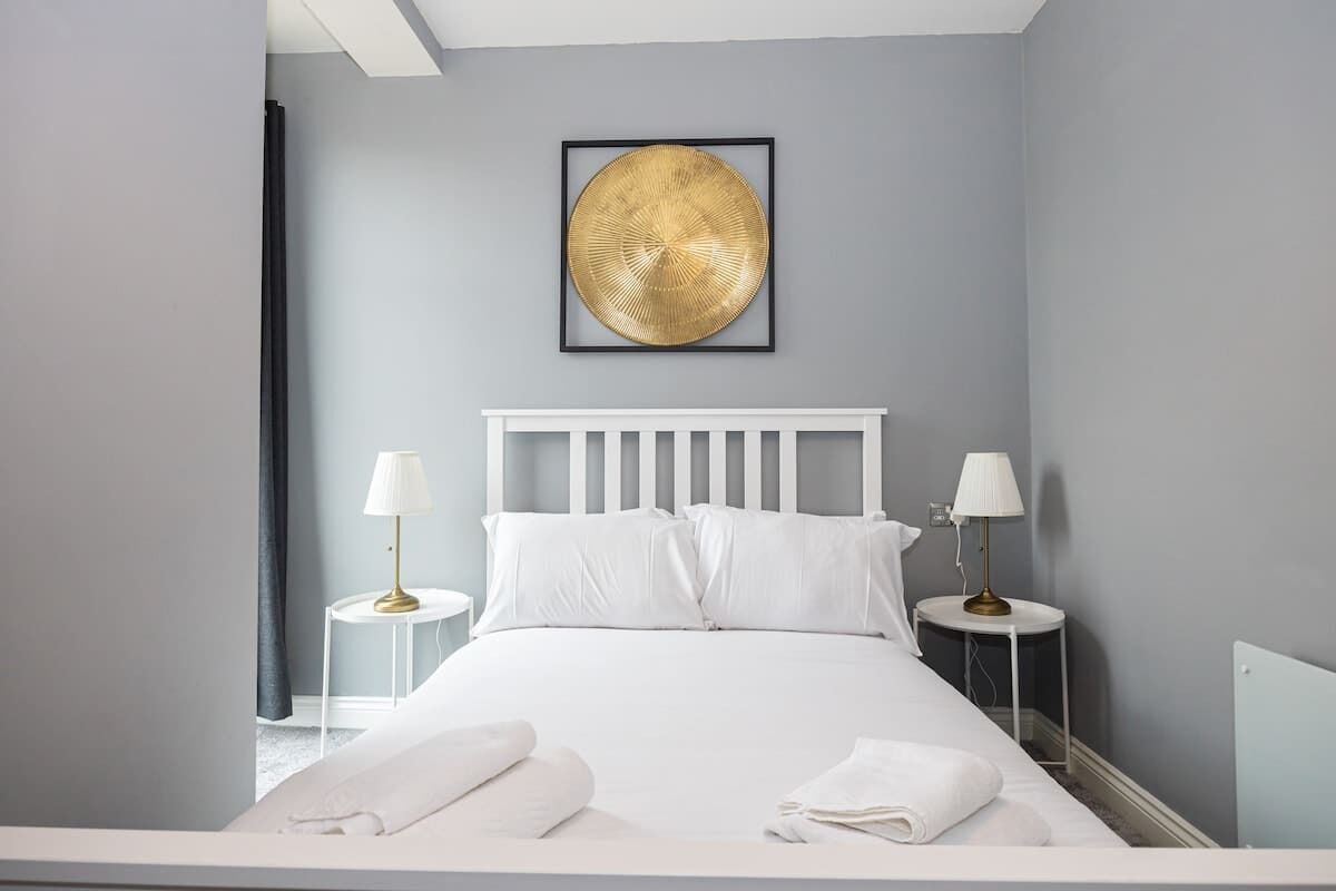 Een keurig opgemaakt slaapkamer met een wit bed, twee nachtkastjes met lampen, en een ingelijste afbeelding aan de muur.