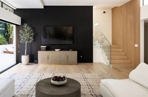Una sala de estar moderna con un televisor de pantalla plana, una planta en maceta y una escalera.