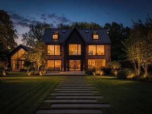 Een modern huis met twee verdiepingen, grote ramen, een verzorgd gazon en een stenen pad naar de ingang.