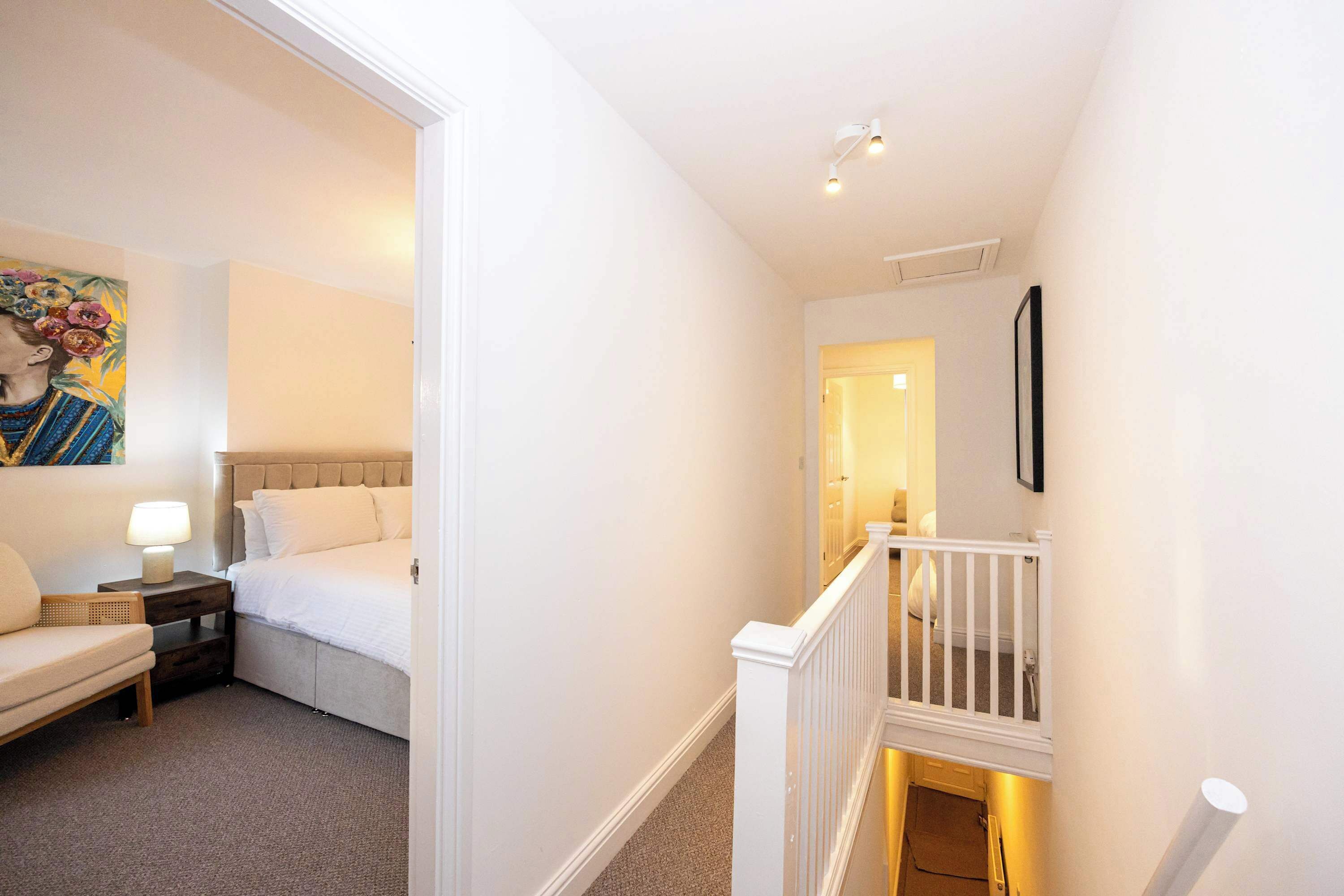 A hotel room with a bed, a nightstand, a lamp, a chair, and a painting on the wall.