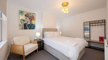 Habitación de hotel con cama, una silla, una mesita de noche con lámpara, un espejo en la pared y un cuadro.