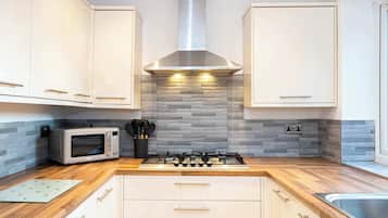 Una cocina moderna con gabinetes blancos, una campana extractora de acero inoxidable, un microondas y una estufa a gas.
