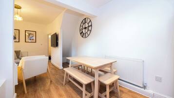 A room with a wooden table and benches, a clock on the wall, and a radiator.
