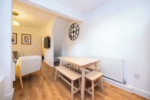 Ein Zimmer mit einem Holztisch, Bänken, einer Wanduhr und einer Heizung.