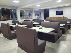 A restaurant with booth seating, tables, and a TV screen on the wall. - Califórnia Suítes (Belo Horizonte)