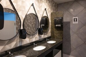 A restroom with three sinks, two hand dryers, and a mirror. - Califórnia Suítes (Belo Horizonte)