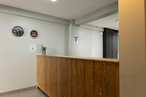 A reception area with a wooden counter, two wall clocks, a fire safety sign, and a small plant. - Califórnia Suítes (Belo Horizonte)