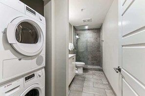 Une petite salle de bain équipée d’un lave-linge, de toilettes et d’une douche.