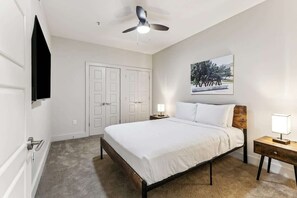 A bedroom with a bed, a ceiling fan, a nightstand, a wall-mounted TV, and a door. - Premier One Bedroom Residence-Sleeps 3 (New Orleans)