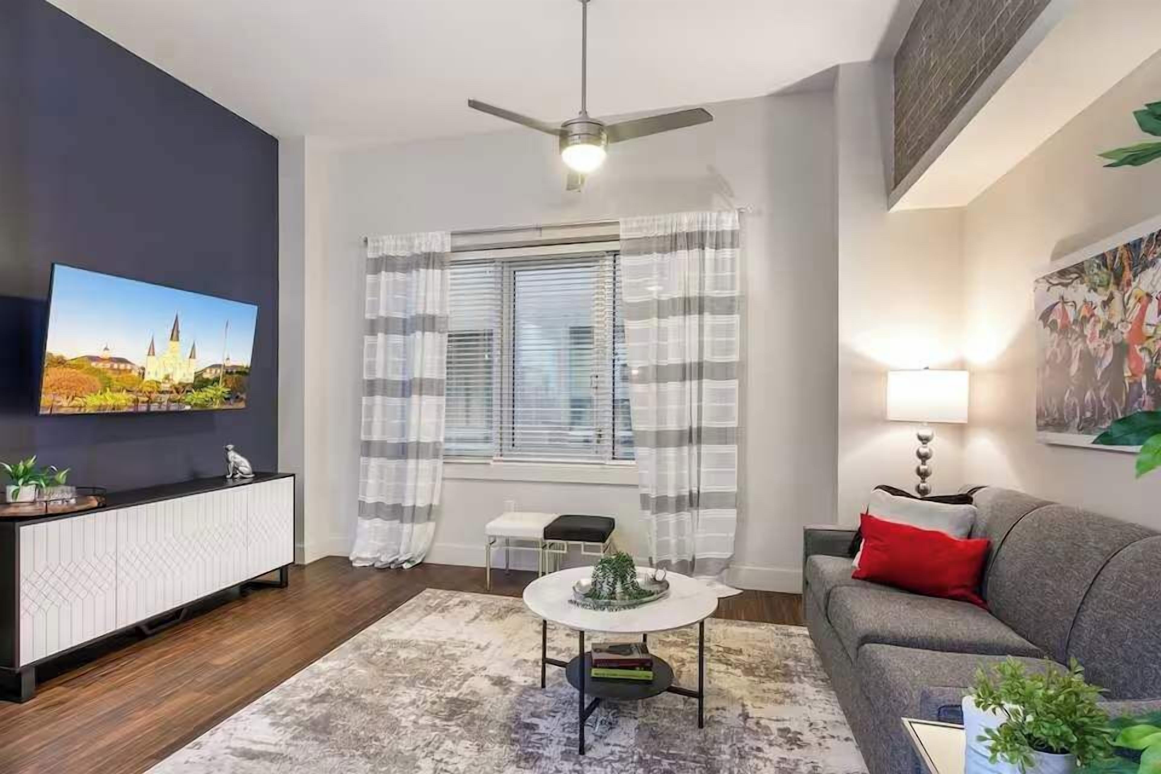 Ein modernes Wohnzimmer mit Sofa, Couchtisch, Fernseher, Deckenventilator und einem Fenster mit Vorhängen.