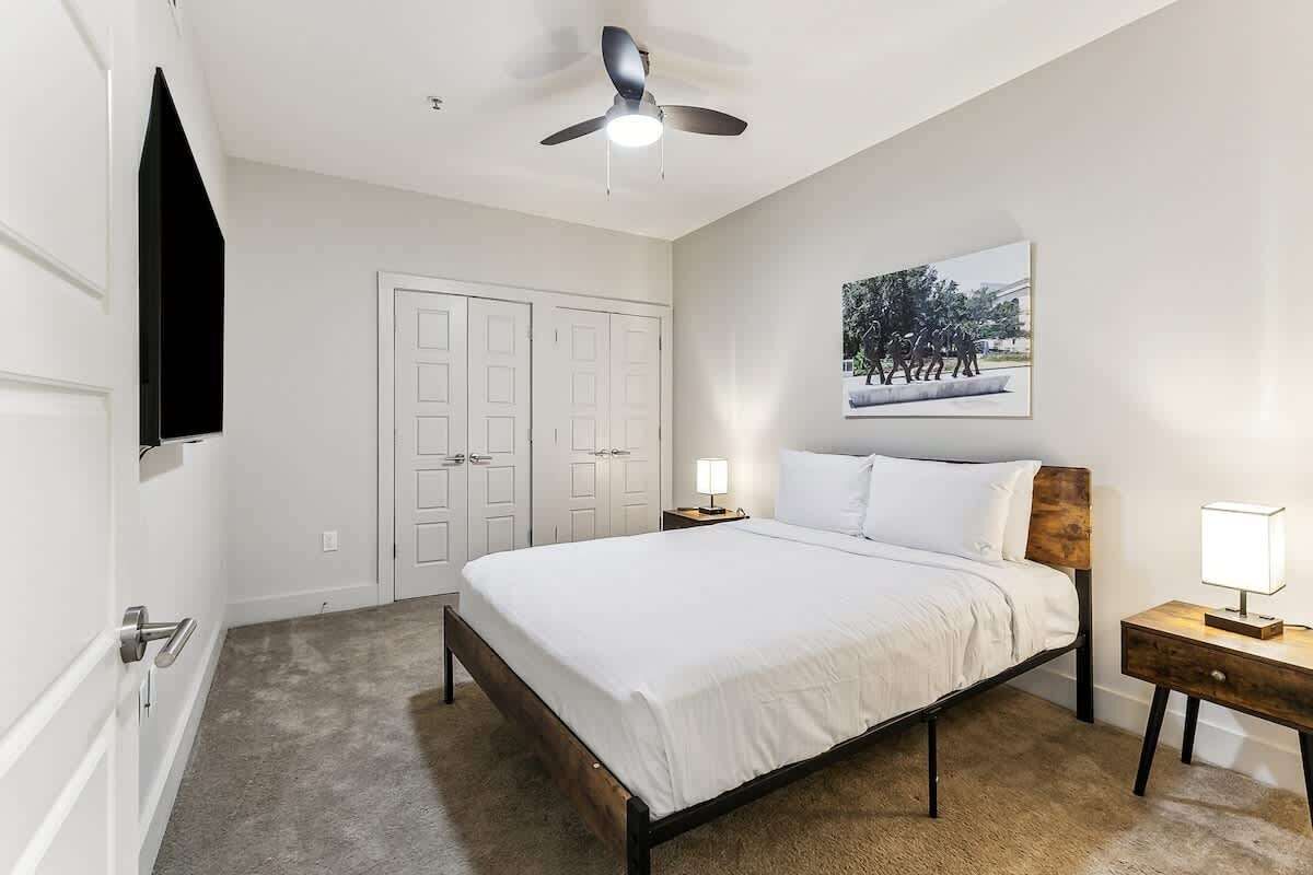 Una camera da letto con un letto, una ventola a soffitto, un comodino, una TV a parete e una porta.