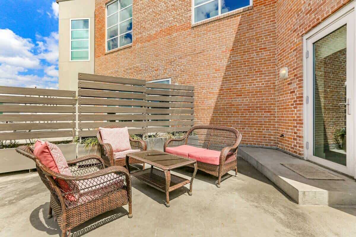 Un patio con mobili in vimini, un tavolo in vetro e un edificio in mattoni sullo sfondo.