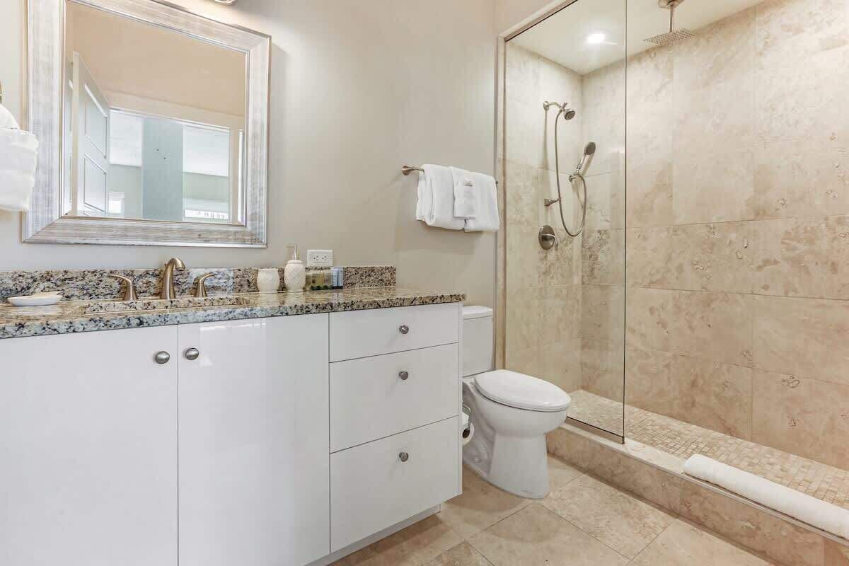 A bathroom with a glass shower enclosure, a white sink with a marble countertop, and a large mirror above the sink.