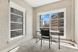 A corner room with a table and chair, large windows, and a view of buildings. - Two Bedroom Penthouse with Balcony-Sleeps 5 (New Orleans)