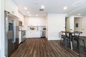 Una cocina moderna con electrodomésticos de acero inoxidable, armarios blancos y piso de madera oscura.