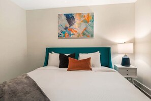 Una habitación de hotel ordenada con cama, mesita de noche, lámpara y un cuadro en la pared.