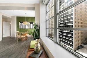 A modern interior with a dining area, a large window with a view of a parking garage, and a green accent wall. - Premier Two Bedroom Residence-Sleeps 5 (New Orleans)