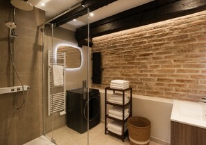 Ein modernes Badezimmer mit Duschkabine aus Glas, integriertem Handtuchhalter, einer schwarzen Waschmaschine und einer Wand aus Naturstein.