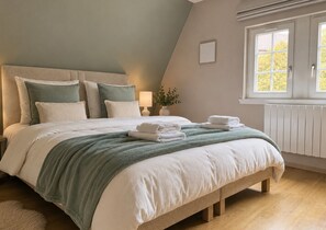 Ein Schlafzimmer mit Bett, Kissen, einem Nachttisch mit Lampe, einem Fenster und einer Heizung.