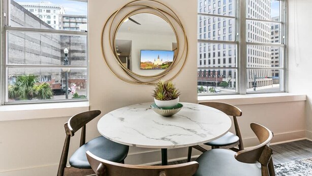 Una habitación con una mesa redonda, sillas, un espejo y una ventana con vista a la ciudad.
